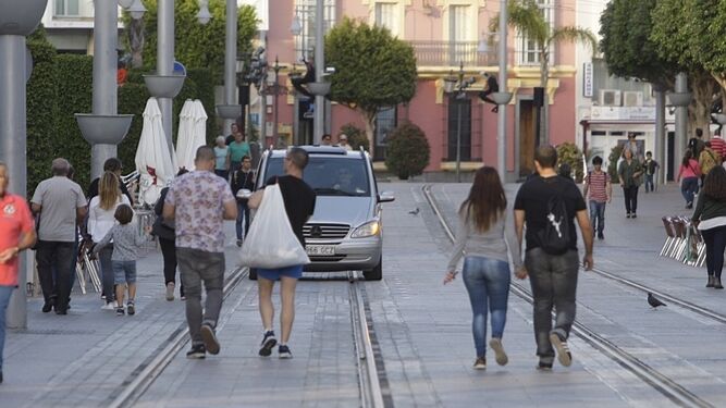 Un vehículo circulando por la calle Real, mientras los peatones transitan por la plataforma tranviaria.