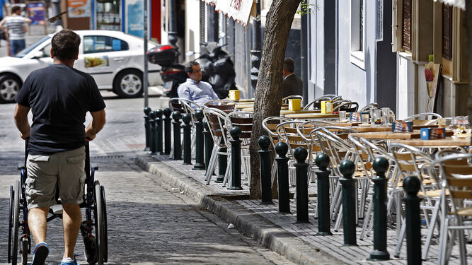 Un hombre transita empujando una silla de ruedas por enmedio de la calzada de la calle Libertad.