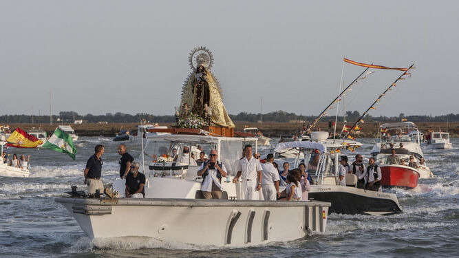 La Virgen del Carmen de Gallineras surca sobre una embarcación con una estela de de barcos el caño de Sancti Petri cuando ya regresa de La Magdalena.