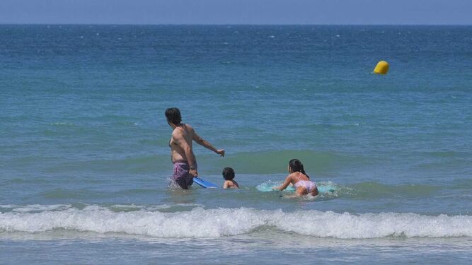 Un padre se da el primer baño con sus hijos en la playa Victoria.