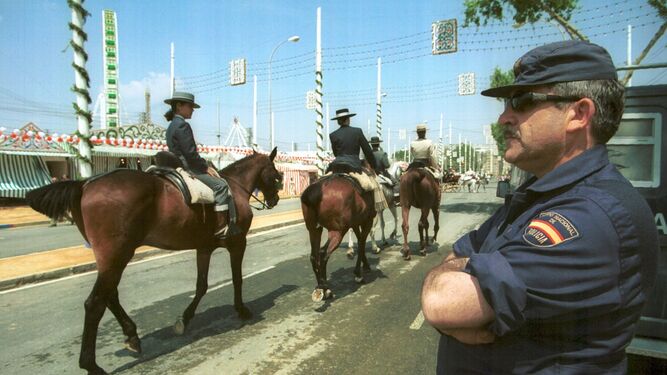 Un agente de la Policía Nacional vigila la Feria mientras pasa un grupo de jinetes y amazonas.