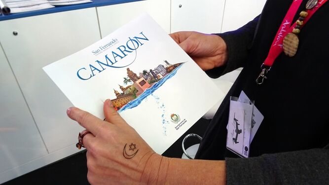 Una trabajadora de la Oficina de Turismo en Fitur, con el material informativo y el tatuaje de Camarón en su mano.