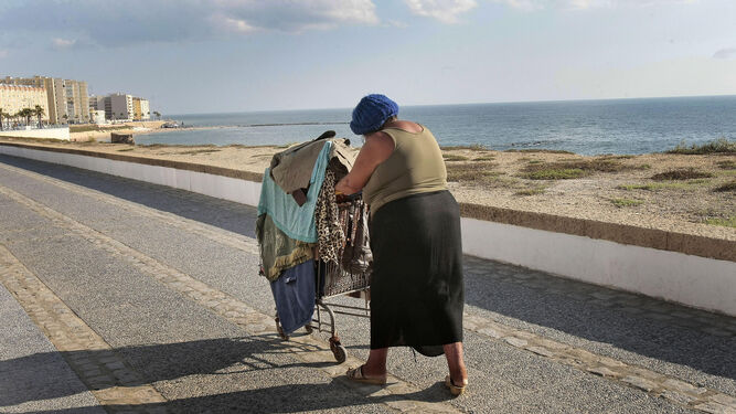 Una mujer sin hogar empuja un carrito con todas sus pertenencias por el paseo marítimo de Cádiz.