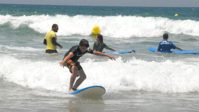 Un joven intenta coger una ola con su tabla de surf en la playa de Cortadura.