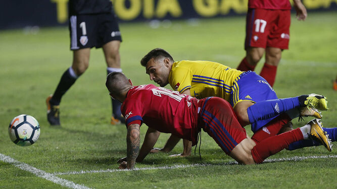 David Barral y un futbolista del Osasuna caen al césped mientras el balón sale del terreno de juego.