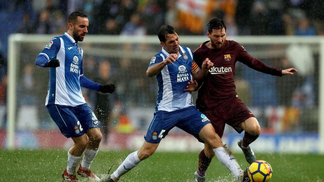 Víctor Sánchez, con Darder detrás, mete su pierna izquierda para cortar el avance de Messi en un terreno de juego encharcado.