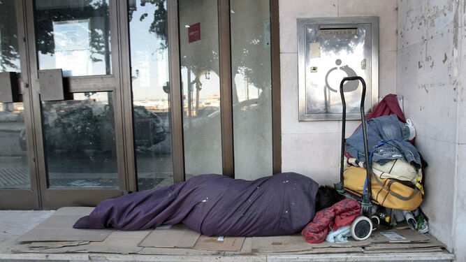 Una persona sin hogar descansa en el portal de un local comercial.