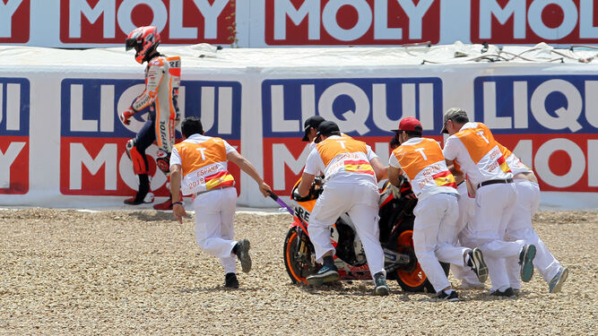 Varios comisarios de pista retiran la Honda 93 de la escapatoria de Dry-Sack mientras Marc Márquez camina cabizbajo.