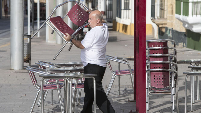Un camarero coloca las sillas de la terraza de un establecimiento hostelero de la calle Real.