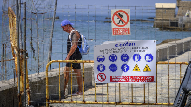 Un hombre accede a la playa de La Caleta detrás de la valla de seguridad de la obra