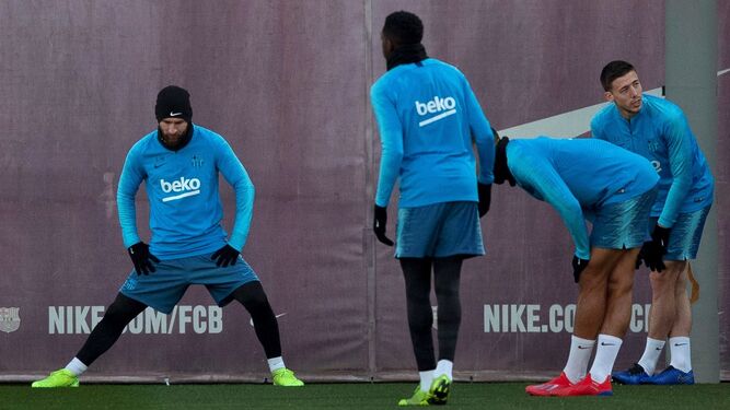 Messi, con gesto serio, estira en el entrenamiento barcelonista con Dembele de espaldas.
