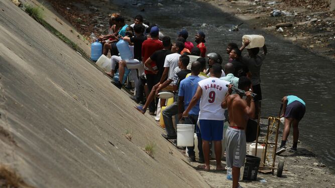 Decenas de venezolanos recogen agua en un río de Caracas tras los apagones.