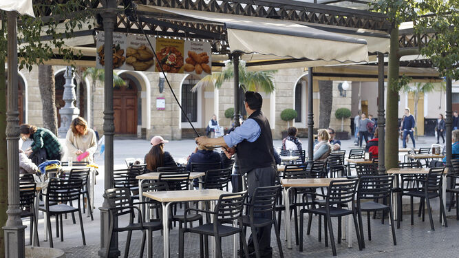 Un camarero recoge un toldo en un bar de la plaza de San Juan de Dios.