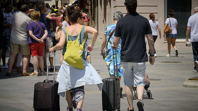 Dos personas con maletas caminan hacia su hospedaje por la plaza de San Juan de Dios.