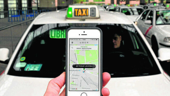 Un usuario consulta la aplicación de Uber delante de un taxi.