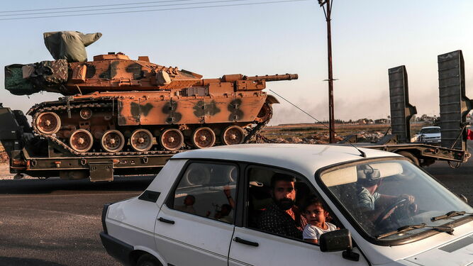 Una familia en su coche frente a la puerta fronteriza de Akcakale mientras los vehículos militares turcos se desplazan hacia el norte de Siria.