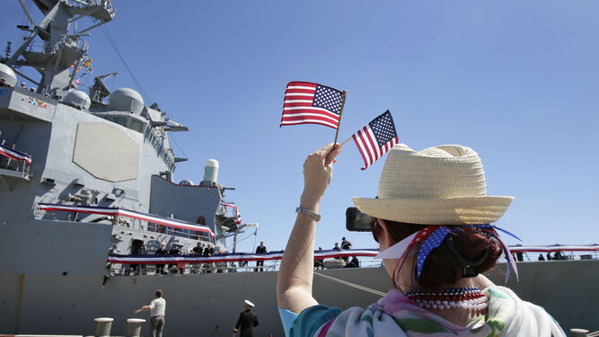 Una ciudadana estadounidense recibe al tercer destructor  ataviada con complementos con los colores de su país y dos banderas norteamericanas.