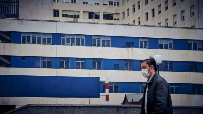 Un hombre camina con una mascarilla por los aleda&ntilde;os del Hospital Puerta del Mar