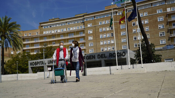 Un hombre y una mujer abandonan el Hospital Virgen del Rocío ataviados con mascarillas.