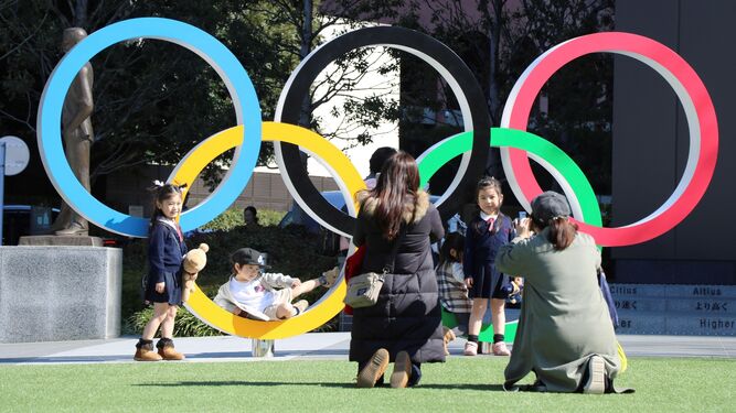 Unos niños posan en Tokio junto a los aros olímpicos.