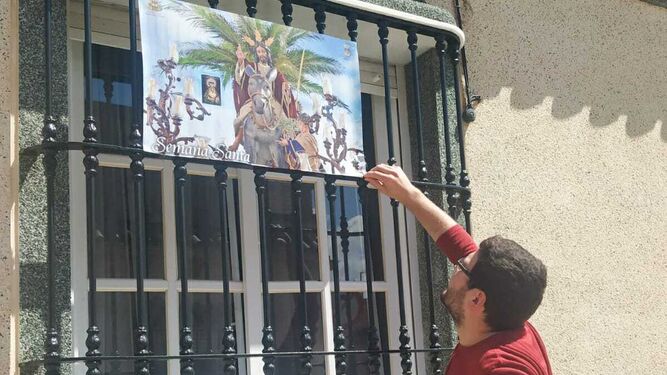 Un vecino cuelga en su ventana un cartel de la procesión de La Borriquita.