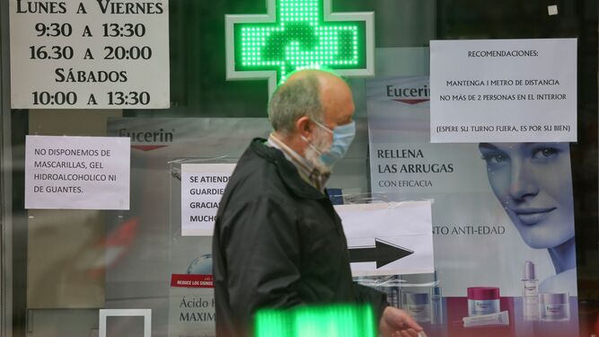Un hombre con mascarilla pasa por delante de una farmacia.
