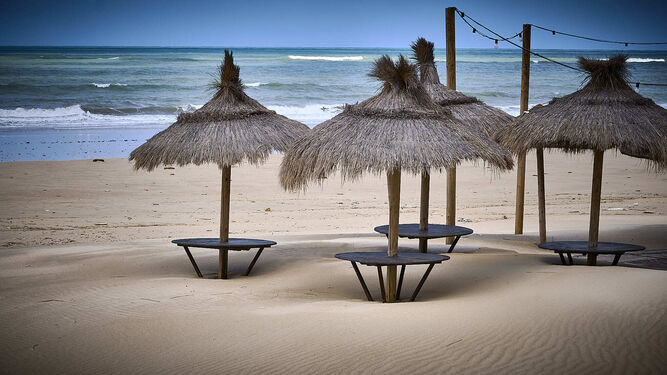 Sombrillas y mesas de un chiringuito de La Victoria, ahogadas por la subida del nivel de la arena.
