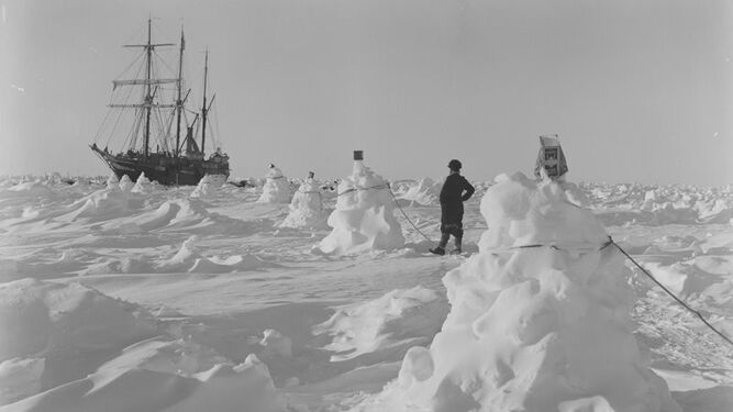 Montones de nieve unidos con cuerdas para servir de guía en las ventiscas, con el 'Endurance' al fondo'
