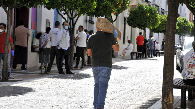 Una persona con un paquete en la calle Corredera, con gente haciendo cola en los bancos.