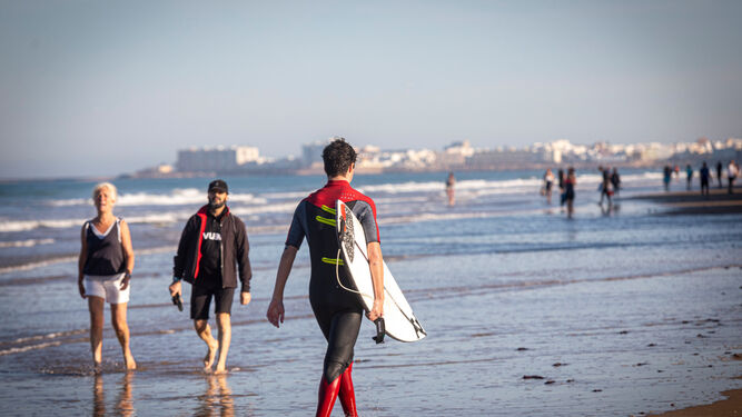 Un surfista, con su tabla, por una playa de Cádiz.