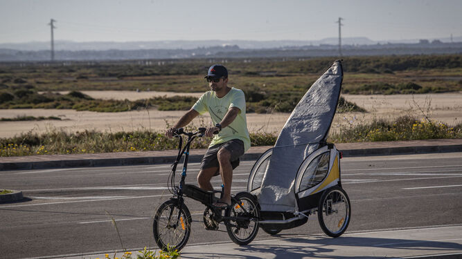 Un surfero en bici y con la tabla en un remolque en los accesos de la playa de Camposoto durante el estado de alarma.