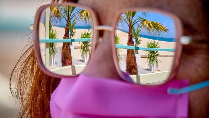 La playa reflejada en las gafas de una mujer con mascarilla.