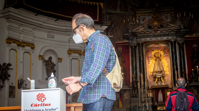 Un hombre con mascarilla se desinfecta las manos con gel hidroalcohólico antes de entrar en la Iglesia de La Palma.