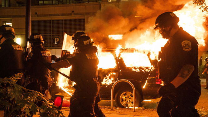 La Policía pasa delante de un coche ardiendo en llamas
