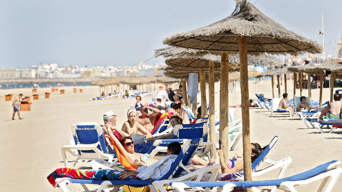 Turistas en tumbonas y sombrillas, ante un hotel, en una playa de Cádiz.