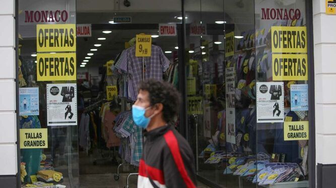 Un joven con mascarilla camina por delante de un negocio del centro  de Chiclana.