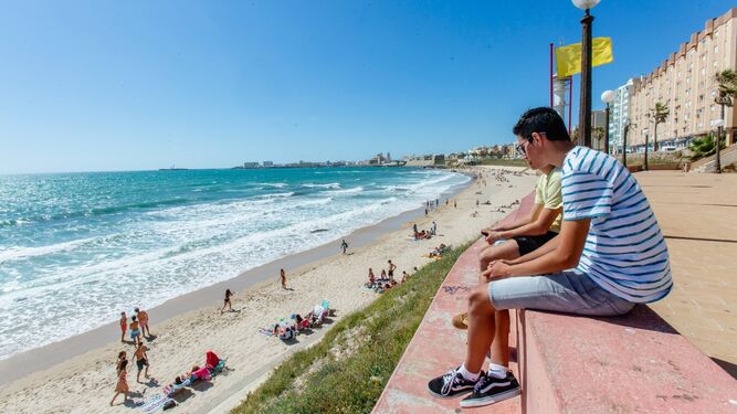 Dos jóvenes observan la playa de Santa María del Mar, con bandera amarilla.