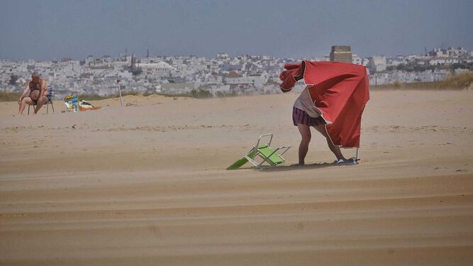 Una persona intentando poner una sombrilla en la playa de El Palmar.