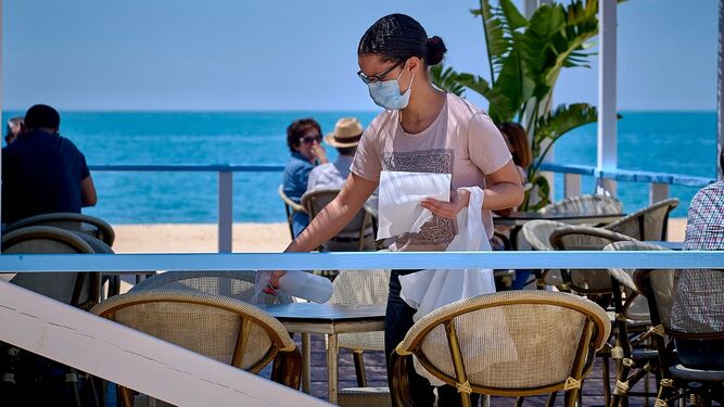 Una camarera limpia una terraza para los siguientes clientes en Cádiz.