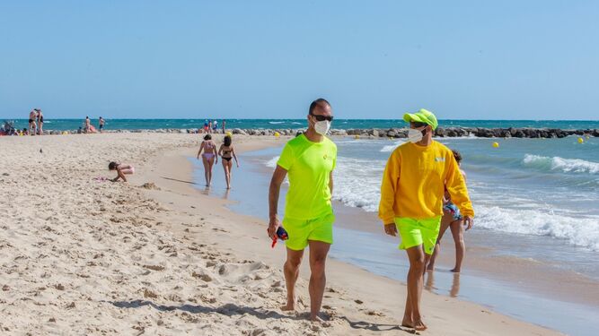 Dos socorristas con mascarillas, por una playa de Cádiz.