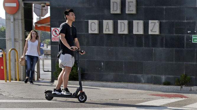 Un usuario de un patinete eléctrico circulando por delante de la entrada principal del Puerto de Cádiz.