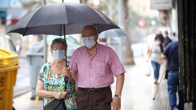 Dos personas andan este lunes por la calle guarecidos de la lluvia con un paraguas.