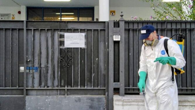 Un operario realizando trabajos de desinfección junto a la puerta de un colegio de Sanlúcar.