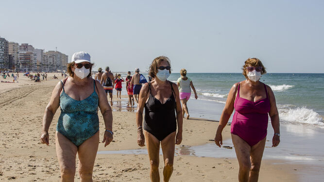 Tres mujeres andan por la orilla en la playa de La Victoria con sus mascarillas.