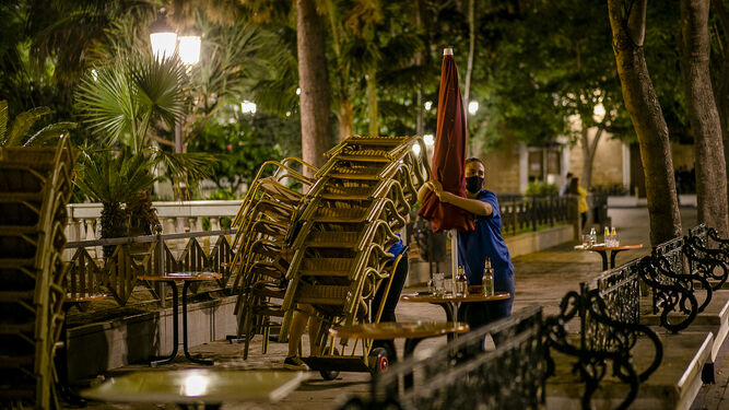 Una camarera recoge las sillas de una terraza en la Plaza de Mina.