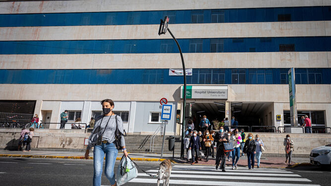 Varias personas cruzan el paso de peatones frente al hospital de Cádiz.