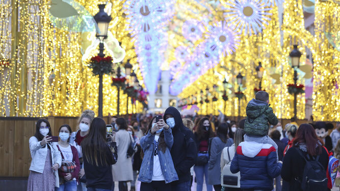 Numerosas personas pasean con mascarilla en una de las calles céntricas de Málaga tras el encendido del alumbrado navideño.