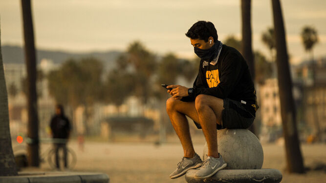 Un hombre con mascarilla consulta su teléfono en Venice Beach, en California.
