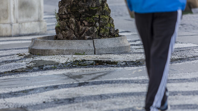 Un hombre camina junto a un alcorque en mal estado y el pavimento deteriorado.