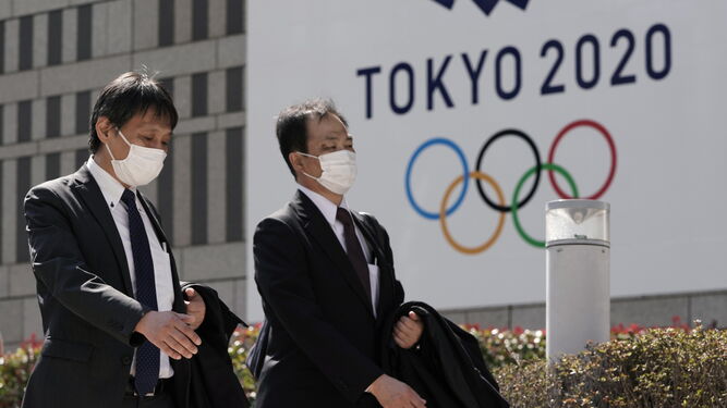 Dos japoneses con mascarillas pasan ante un cartel anunciando los JJOO de Tokio